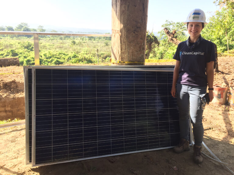 Woman in CleanCapital shirt holding solar panel at construction site overlooking green landscape