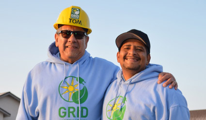 Two men wearing yellow hard hat and blue GRID hoodies smile together outdoors
