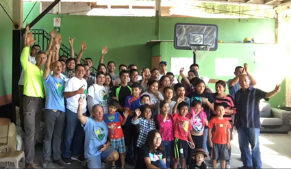 Large group of adults and children posing together indoors, celebrating GRID's first project in Mexico