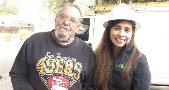 Two people smiling outdoors next to a work truck, man wearing San Francisco 49ers shirt, woman in hard hat