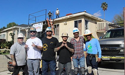 Group of seven people in hard hats standing in front of a house with solar panels being installed on the roof
