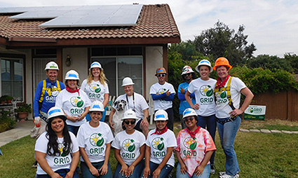 Group of GRID interns wearing hard hats and GRID t-shirts posing outside a house