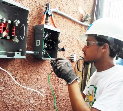 Electrician installing solar panel wiring on exterior wall while wearing safety helmet and gloves