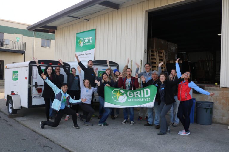 GRID Alternatives team celebrates at winter warehouse event with green banner and white vehicle