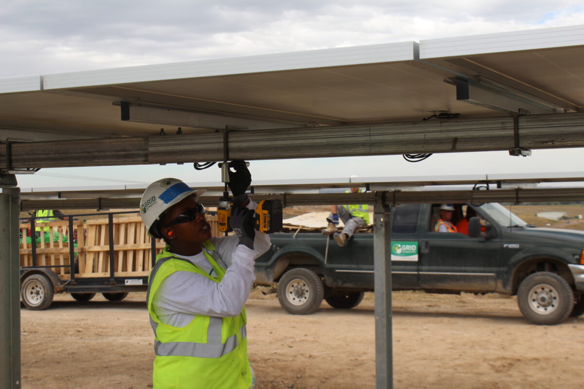 Construction worker installing solar panel mounting system on rooftop structure at job site