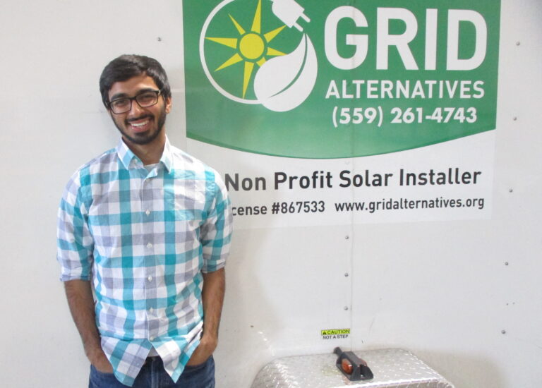 Man in blue plaid shirt standing in front of Grid Alternatives nonprofit solar installer sign