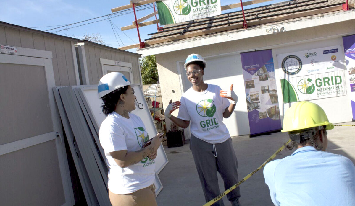 GRID Alternatives staff members in white shirts and hard hats discuss solar installation project at community event