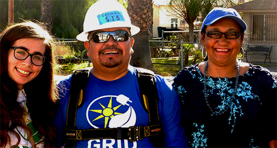 Three smiling people outdoors wearing caps and glasses, one in GRID branded blue shirt