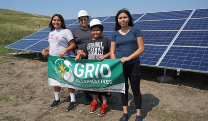Four people holding a GRIO Alternatives banner in front of solar panels in a field