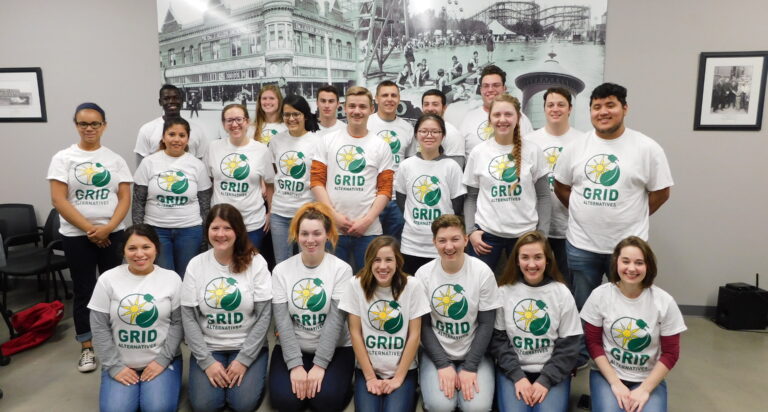 GRID Alternatives team in white shirts with logo, group photo at indoor venue with historic amusement park backdrop