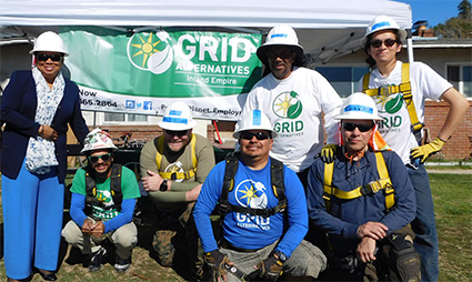 Group of volunteers in hard hats at GRID Alternatives community solar event, holding banner with organization logo