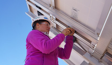 Navajo woman in hard hat installing solar panel on roof