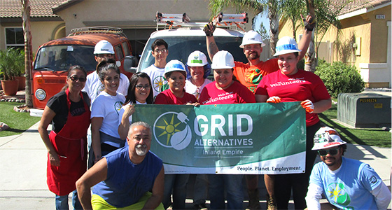 Group of volunteers in hard hats holding GRID Alternatives banner at a residential home