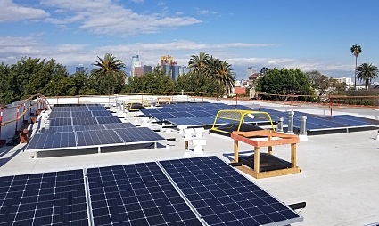 Rooftop solar panel installation on a building with city skyline and palm trees in background