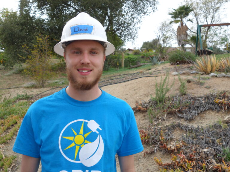 Man named David in hard hat and blue shirt at garden site with solar logo