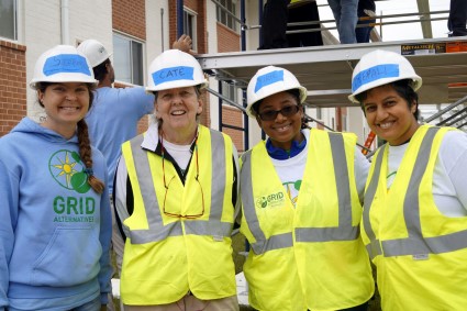 Four women in hard hats and safety vests smile at a construction site