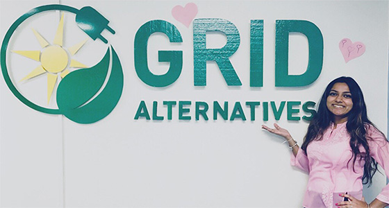 Grid Alternatives logo with solar panel icon and woman in pink shirt smiling at camera