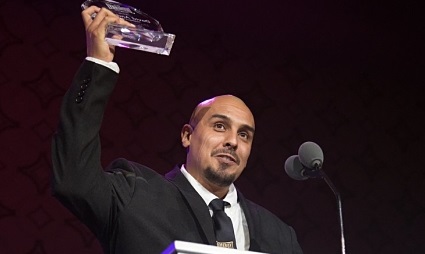 Man in suit holding award at microphone during Lo Maximo event