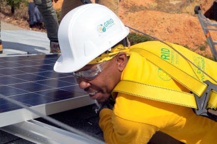 Worker installing solar panel wearing white hard hat and yellow safety vest