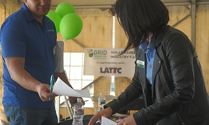 Two people exchanging materials at a career fair with green balloons and LATTC signage visible