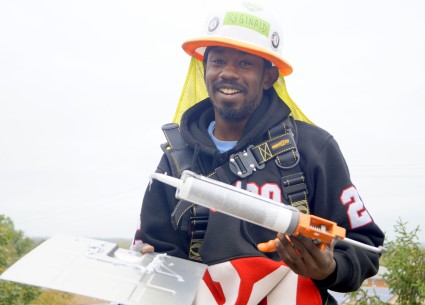 Man in construction gear holding caulk gun, smiling at camera outdoors