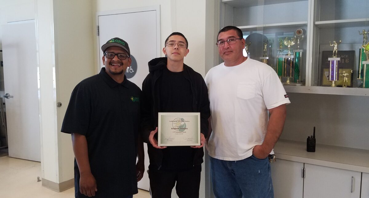 Three men holding a certificate in front of trophy display case, representing solar energy leadership award recipients