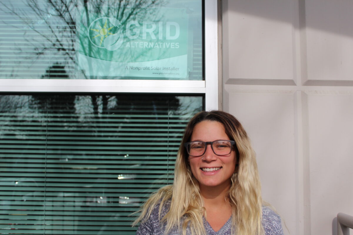 Brittany Heller smiling at GRID Alternatives office with logo visible on window behind her
