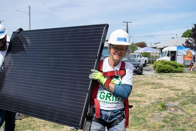 Worker in safety gear holding a solar panel at an outdoor green energy event
