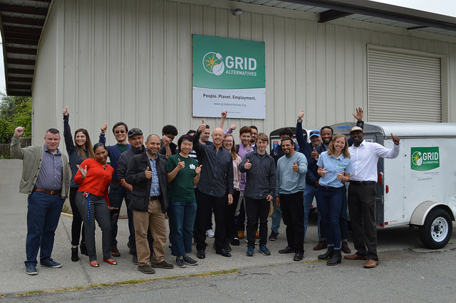 Group of GRID Alternatives trainees celebrating outside building with solar trailer