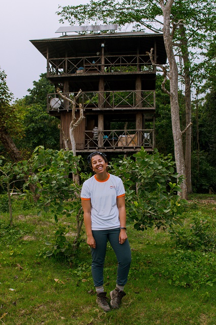 Man in white shirt standing before a multi-level wooden observation tower surrounded by jungle vegetation in Nepal