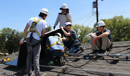 Workers in hard hats install rooftop solar panels on a residential home on a sunny day