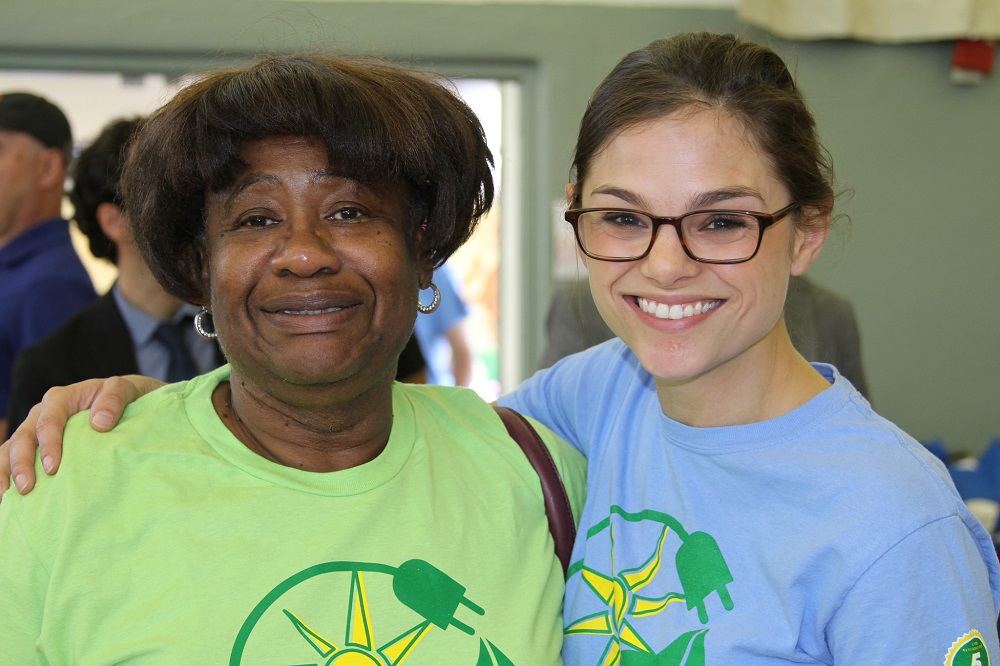 Two women smiling together at an indoor event, wearing matching green and blue t-shirts with environmental graphics