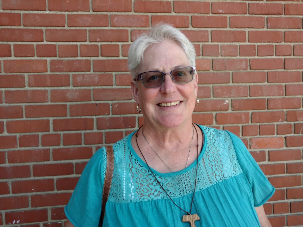Smiling woman wearing turquoise lace top and sunglasses against brick wall
