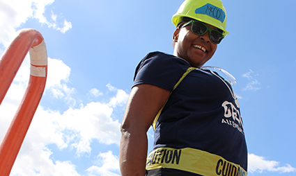 Construction worker in safety gear smiling at camera with "Caution" tape visible