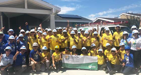 Large group wearing yellow shirts and hard hats at solar panel installation event holding Sunrun banner