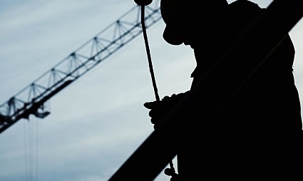 Silhouette of construction worker on rope with crane in background