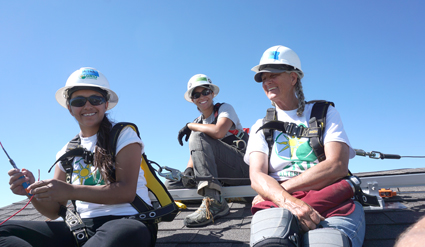 Three students in hard hats and safety vests work on a solar panel installation at Pine Ridge