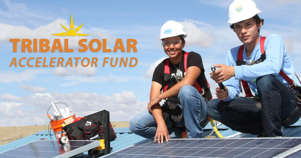 Two workers in hard hats examine solar panels with Tribal Solar Accelerator Fund logo and sun graphic overhead
