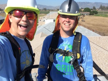 Two women on a rooftop wearing safety gear smile while celebrating work anniversaries at GRID