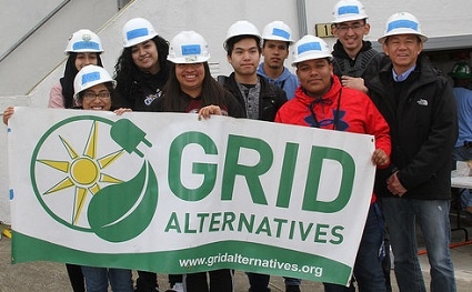Group of people wearing hard hats holding GRID Alternatives banner outdoors