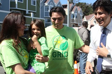 People at solar installation event wearing green GRID Alternatives shirts outside residential buildings