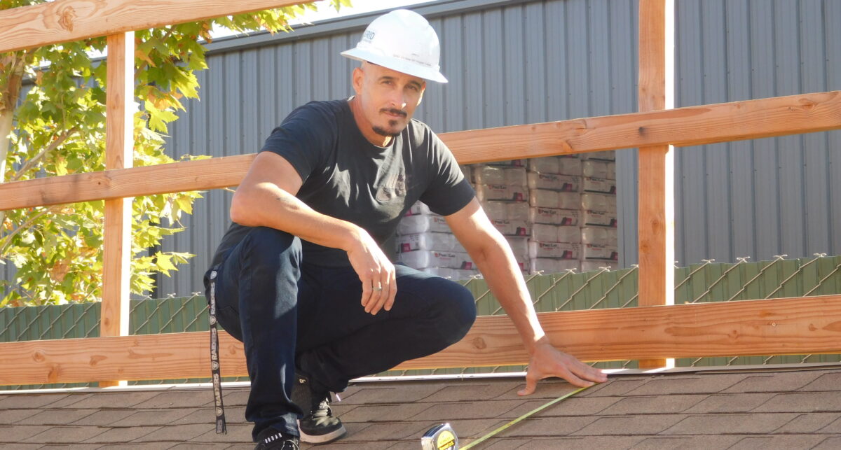 Construction worker in white hard hat crouching on wooden deck with measuring tape