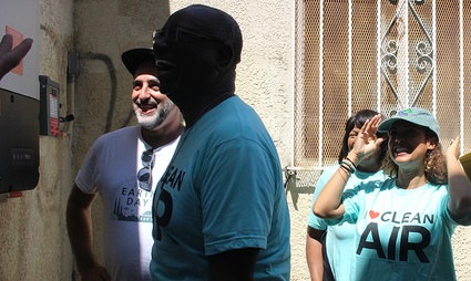 Group of people celebrating solar installation in Watts neighborhood, with person wearing "Clean Air" shirt visible