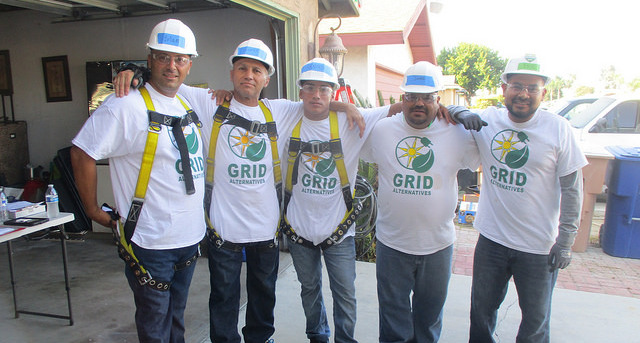 Five workers in hard hats and GRID safety gear pose together at a construction site