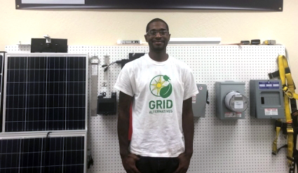 Man wearing GRID t-shirt standing in front of solar panels and electrical equipment in a training facility