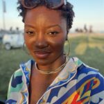 Woman with curled hair wearing brown sunglasses and colorful patterned shirt outdoors