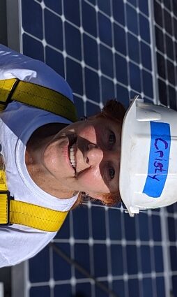 Worker in hard hat and safety vest with solar panels in background
