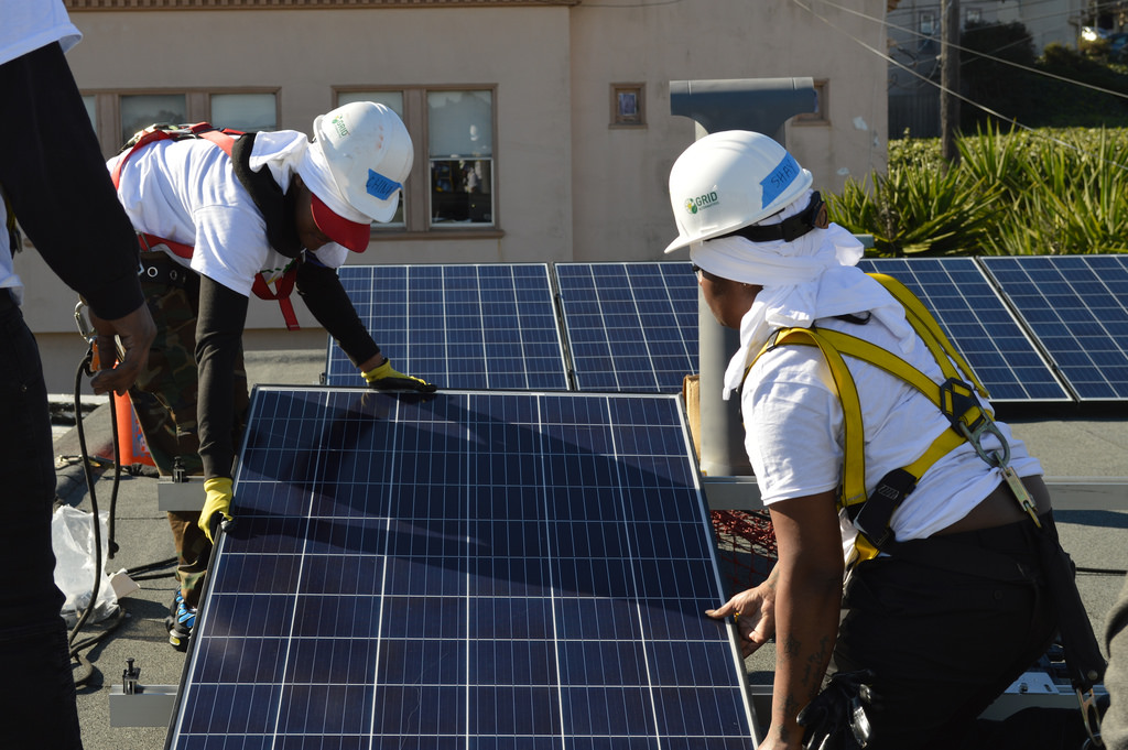Two women from the YCD job training cohort align a solar panel on the roof of a San Francisco residence.