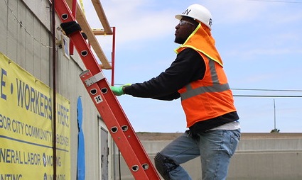 Construction worker in safety gear climbing red ladder on building site