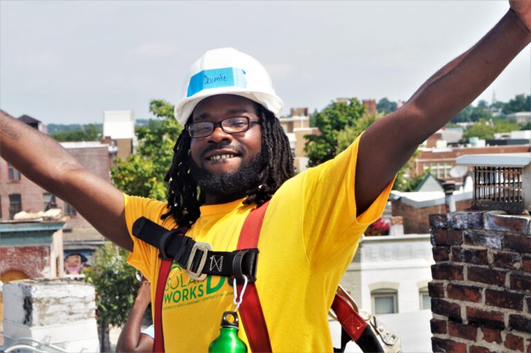 Devonte, a Solar Works DC trainee, puts his arms in the air while on the roof during a solar installation.